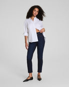 Woman wearing a white shirt and dark blue jeans on a light gray background
