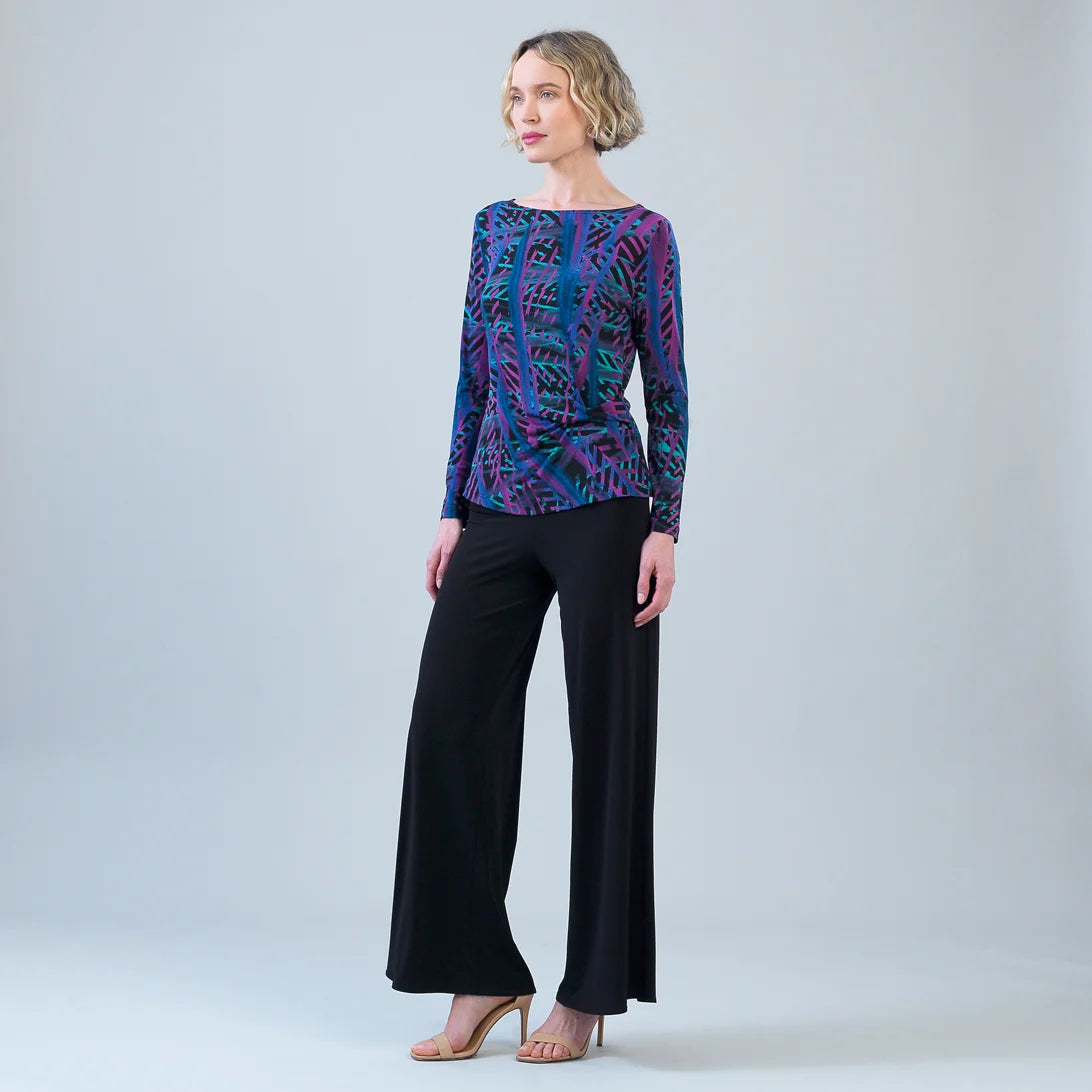Woman wearing a patterned top and black pants on a plain background