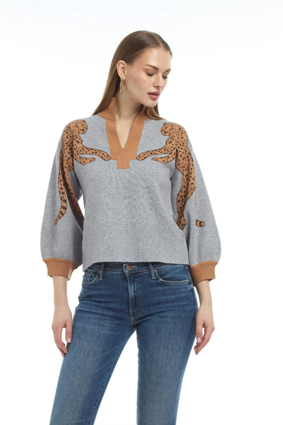 A woman modeling a light gray knit sweater with brown and black leopard print details on the shoulders and sleeves, paired with blue jeans against a plain white background.