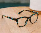 Peepers Betsy cat eye reading glasses in Teal Botanico resting on a wood tabletop