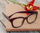 Peepers Center Stage reading glasses in Dark Cherry, styled flat lay