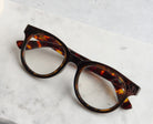 Peepers Olympia reading glasses in Coffee Tortoise resting on marble