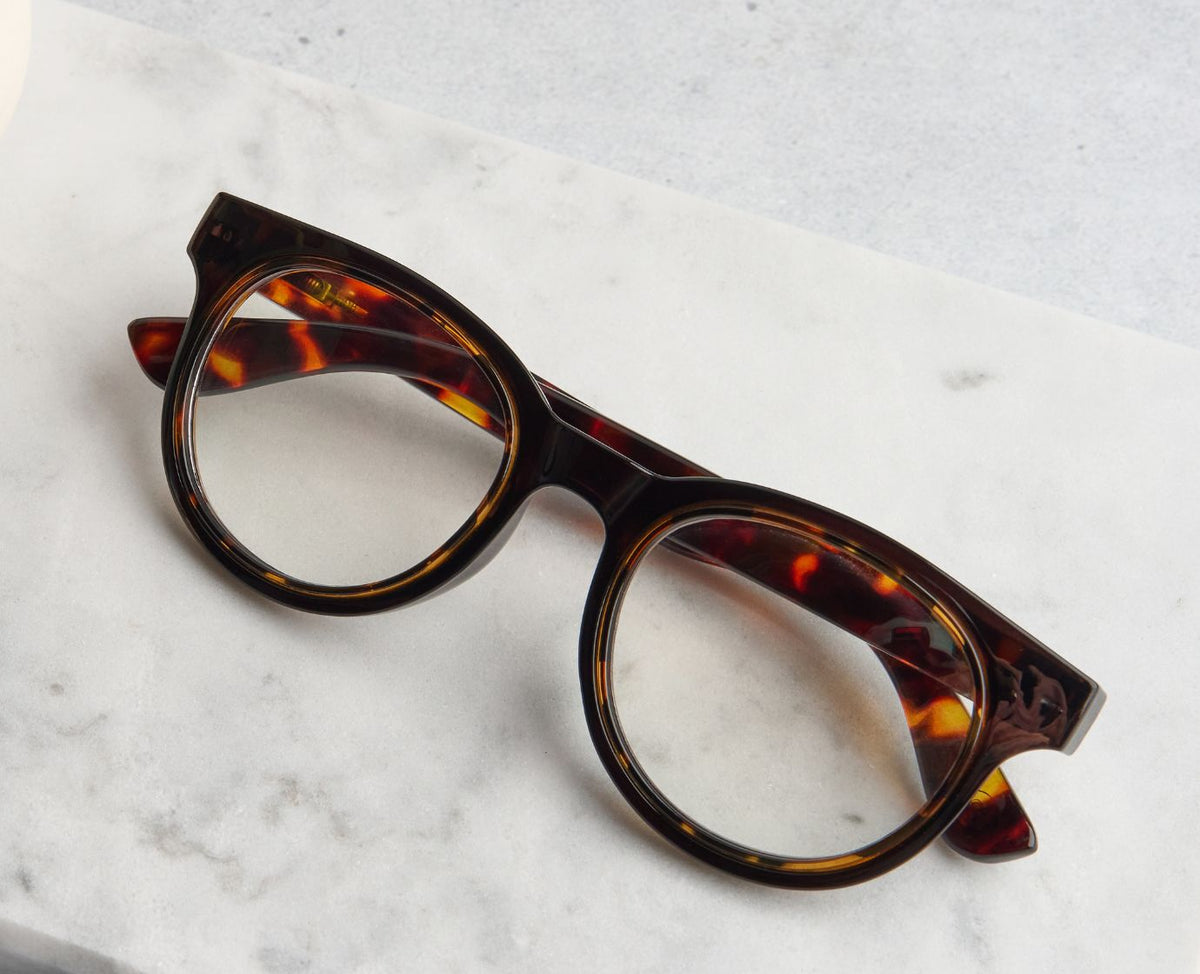 Peepers Olympia reading glasses in Coffee Tortoise resting on marble