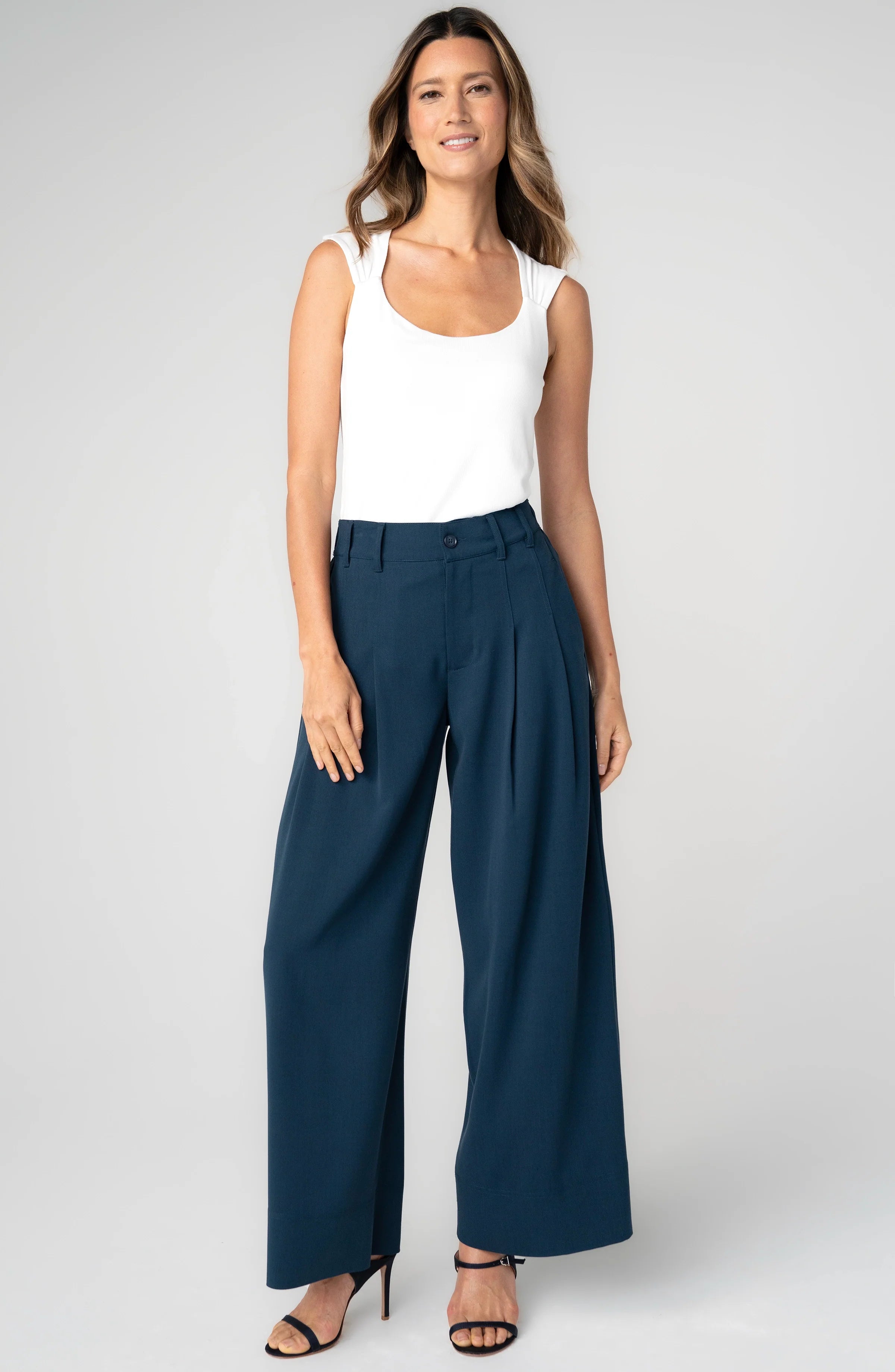 A model wearing pleated wide leg trousers in oxford navy with a high-rise fit.