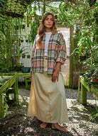 prAna Cabin Core Flannel Shirt in multi plaid sage, rust and cream, worn open over a white tee with a sage satin midi skirt in a greenhouse