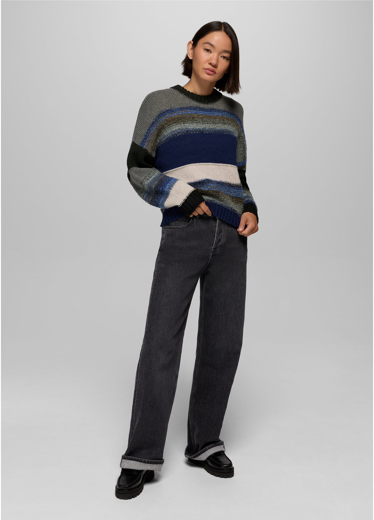 Model wearing the prAna Carlsbad High Rise Wide Leg jeans in Black Sand with a striped crewneck sweater and black loafers, cuffed at the hem