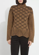 A woman modeling a camel and black chevron-knit turtleneck pullover with a scalloped hem, ribbed sleeves, and black trousers, against a plain light gray studio background.