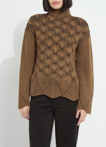 A woman modeling a camel and black chevron-knit turtleneck pullover with a scalloped hem, ribbed sleeves, and black trousers, against a plain light gray studio background.