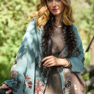 A woman wearing a SAACHI Bloom Reversible Fur Scarf, a light blue floral watercolor print wrap with a plush dark faux-fur trim, draped over her shoulders.