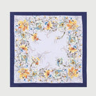 A SAACHI floral oversized bandana laid flat, featuring a navy blue border and an orange, yellow, and blue floral wreath pattern on a pale lavender background.
