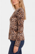 A woman wearing a long-sleeve crewneck sweater with a brown and beige leopard print, paired with dark blue jeans, shown from a side profile against a light gray background.