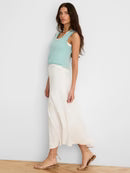 Woman wearing a light blue sleeveless top and white pants against a plain background