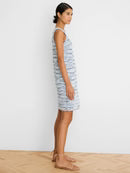 Woman wearing a striped dress standing on a wooden floor with a white wall background
