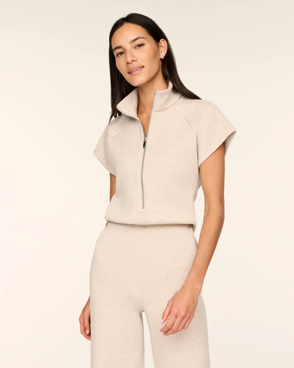 Close-up of a woman wearing the Spanx AirEssentials Pintuck Half Zip Jumpsuit in Bone Heather, showing the stand collar, silver half-zip front and short cap sleeves