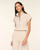 Close-up of a woman wearing the Spanx AirEssentials Pintuck Half Zip Jumpsuit in Bone Heather, showing the stand collar, silver half-zip front and short cap sleeves