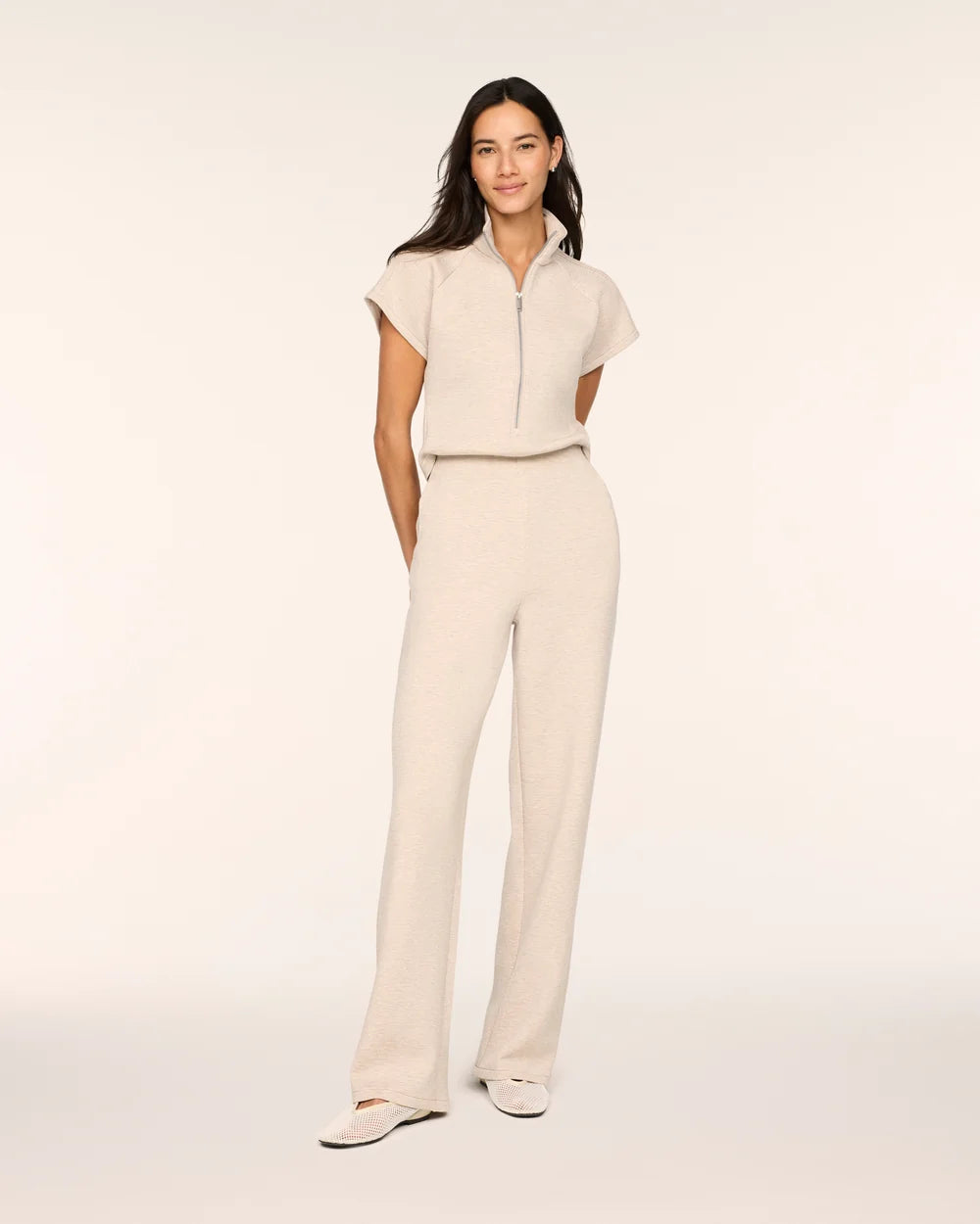 Full-length front view of a woman wearing the Spanx AirEssentials Pintuck Half Zip Jumpsuit in Bone Heather with short sleeves, half-zip collar, pintucked relaxed wide legs and ballet flats
