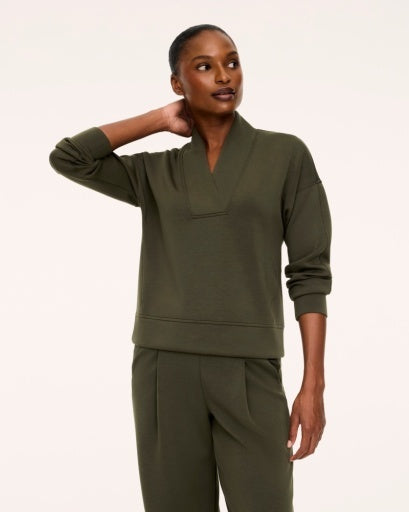 Woman wearing the Spanx AirEssentials V-Neck Long Sleeve Top in Monstera olive green with a wide-collar V-neckline, dropped shoulders, banded cuffs and hem, styled with matching green trousers