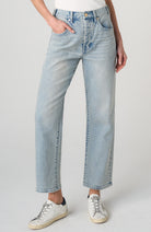 A person wearing light-wash blue straight-leg jeans with a white top and white sneakers, shown from the waist down against a light gray studio background.