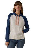A woman wearing a two-tone raglan hoodie with a cream-colored body and navy blue sleeves and hood, featuring peach drawstrings, paired with blue jeans against a white background.
