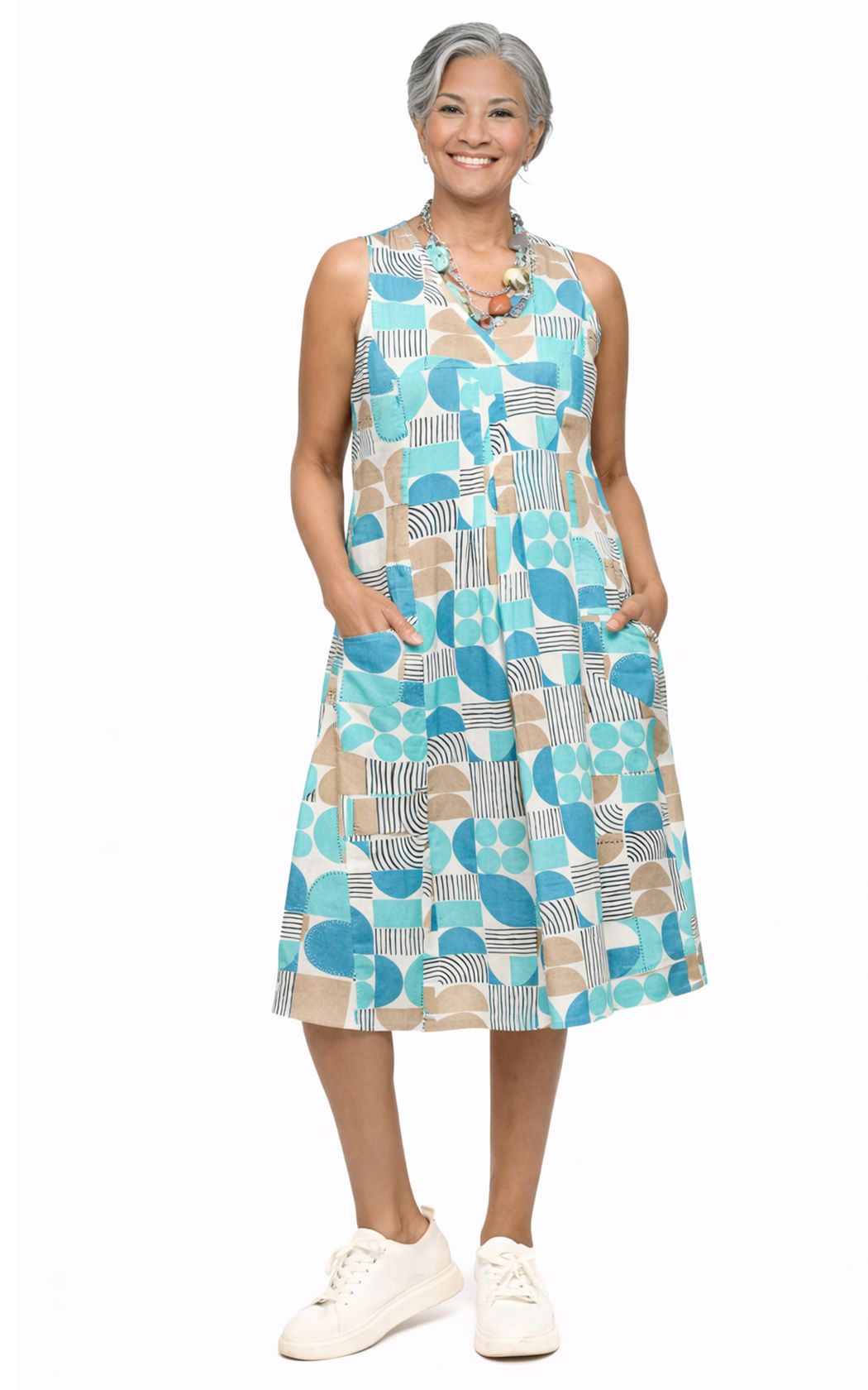 Tulip Clothing Women's Poppie Dress in Geo Candy, woman wearing a sleeveless midi dress with a teal, tan, and white geometric circle print and white sneakers, on a white background