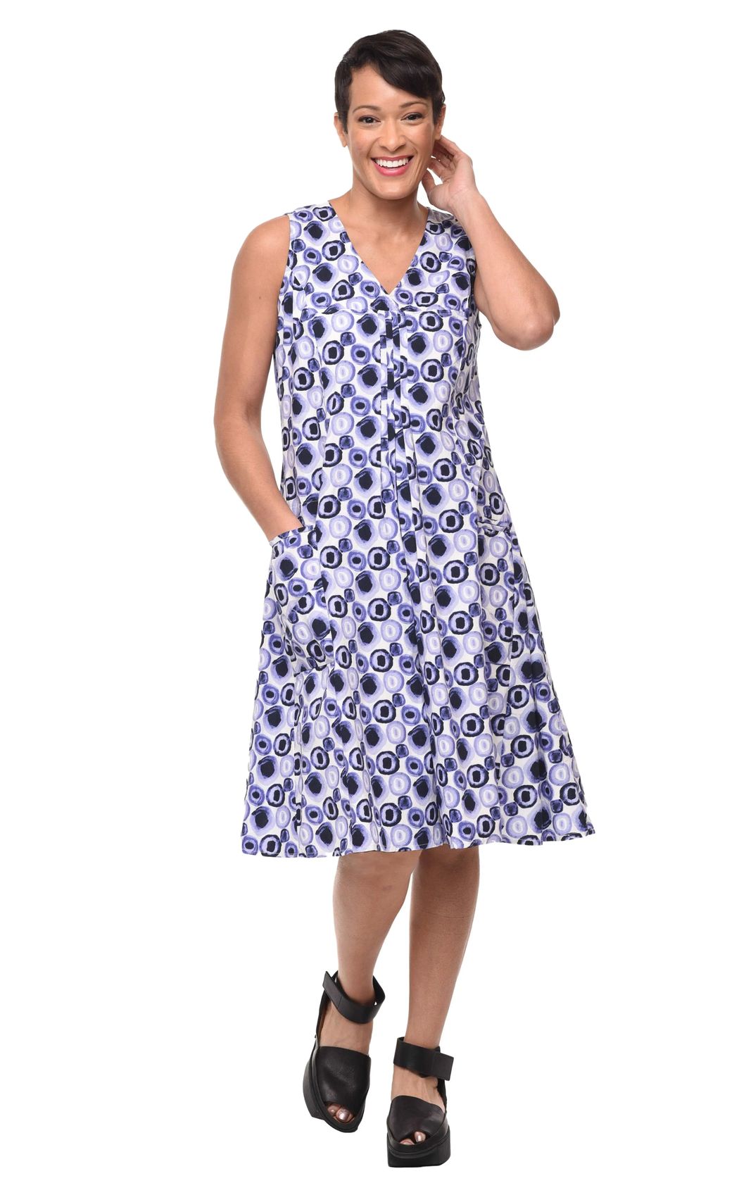 Tulip Clothing Women's Poppie Dress in Iris, woman modeling a sleeveless V-neck midi dress with a blue, black, and white eye-like circular pattern, paired with black platform sandals, against a solid white background
