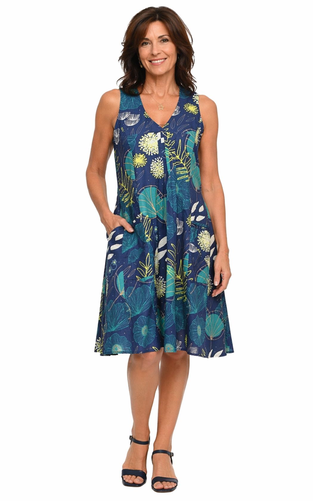 Tulip Clothing Women's Poppie Dress, woman modeling a sleeveless V-neck midi dress with a navy blue and teal tropical leaf print, paired with black sandals, against a white background