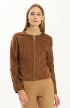 Close-up of the Tyler Böe Piper punched faux suede jacket in Bison brown showing the perforated texture and gold front zipper, styled with a beige turtleneck and tan pants