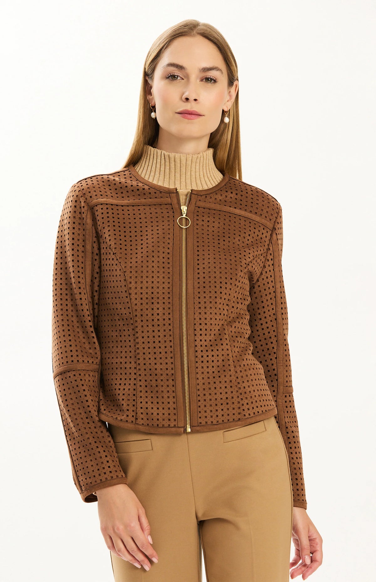 Close-up of the Tyler Böe Piper punched faux suede jacket in Bison brown showing the perforated texture and gold front zipper, styled with a beige turtleneck and tan pants