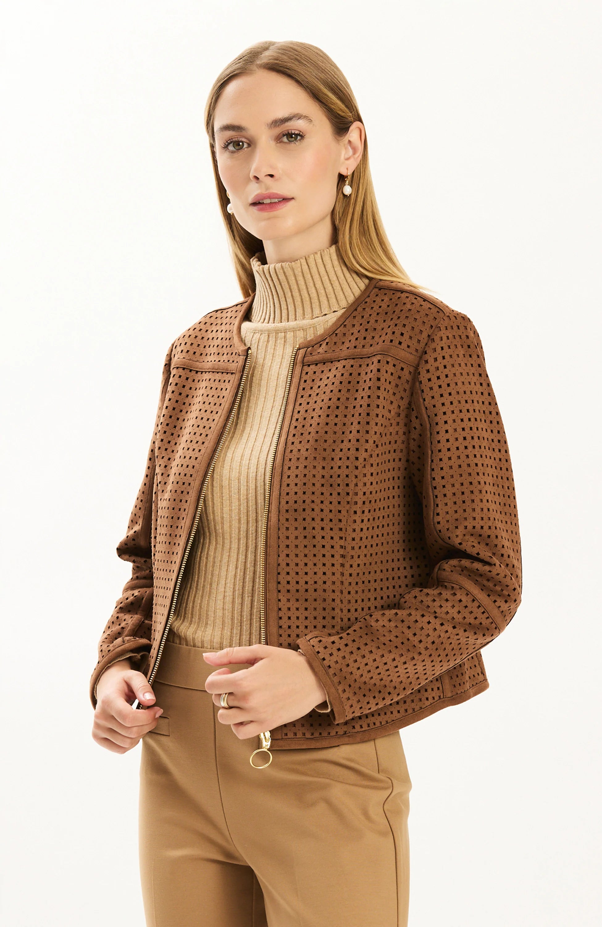 Woman wearing the Tyler Böe Piper punched faux suede jacket in Bison brown, zipped over a beige ribbed turtleneck with tan pants, front view