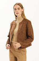 Woman wearing the Tyler Böe Piper punched faux suede jacket in Bison brown, zipped over a beige ribbed turtleneck with tan pants, front view