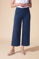 A model wearing dark blue cropped wide-leg pants with a white top and beige wedge sandals, standing against a solid beige background.