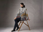 Winding River Floral Fields Asymmetric Travel Coat in dove gray with yellow and blue wildflower print at the hem, worn by a seated model