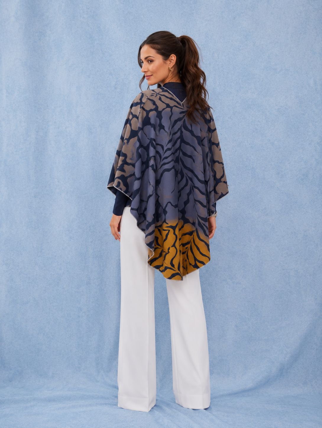 Winding River Marsh Fern Reversible Loop Wrap in navy and slate fern print with camel reverse side, shown from the back with white trousers
