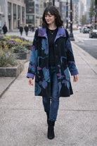 Winding River Reversible Coat from the Lotus Collection in black with purple and teal lotus print and purple collar, worn walking on a city sidewalk