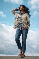 Winding River Wild Lilies Reversible Zipper Sweater in cream with golden yellow and navy lily print, worn with cropped jeans against a blue sky