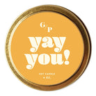 A round gold tin soy candle with a mustard yellow label that reads 'G/P yay you! SOY CANDLE 4 OZ.' on a white background.