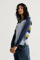 Side view of the Zaket & Plover Color Theory V, a color-blocked V-neck in navy and soft blue with striped sleeves, styled with dark jeans