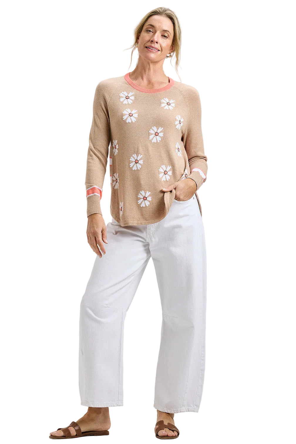 Woman wearing the Zaket & Plover Daisy Chain Sweater, a relaxed tan crew neck knit with white daisies down the front and coral-trimmed cuffs, styled with white wide-leg jeans and sandals