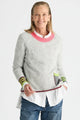 Woman wearing the Zaket & Plover Studio Pop Sweater in Lt Marl, a soft grey knit with a pink crew neck and striped cuffs, layered over a white shirt with blue jeans